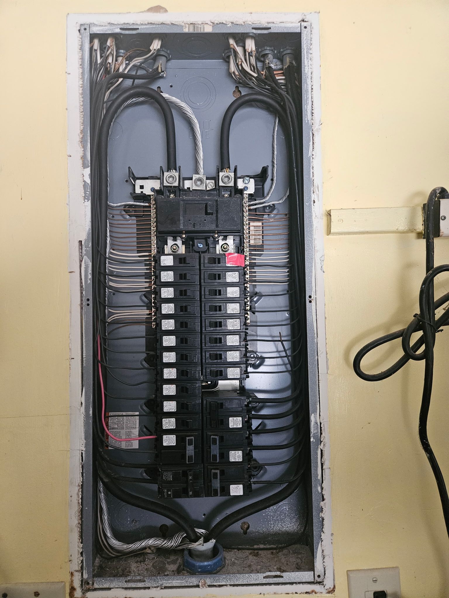 Interior of a breaker panel with the cover removed, showing the main breaker, two rows of branch breakers and neatly routed circuit conductors