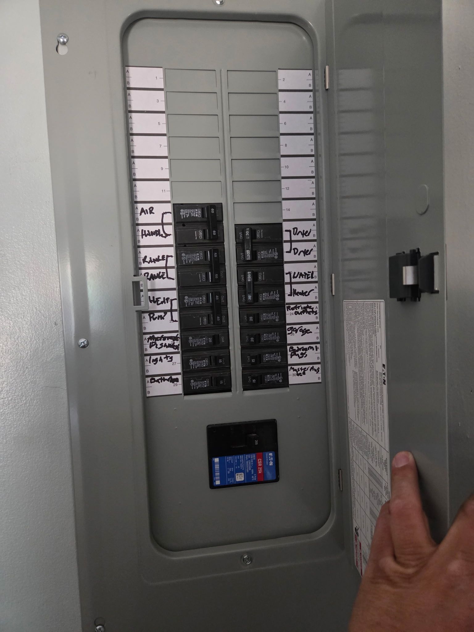 Open Eaton breaker panel with a hand-written circuit directory labelling air handler, range, heat pump, dryer, water heater and room circuits