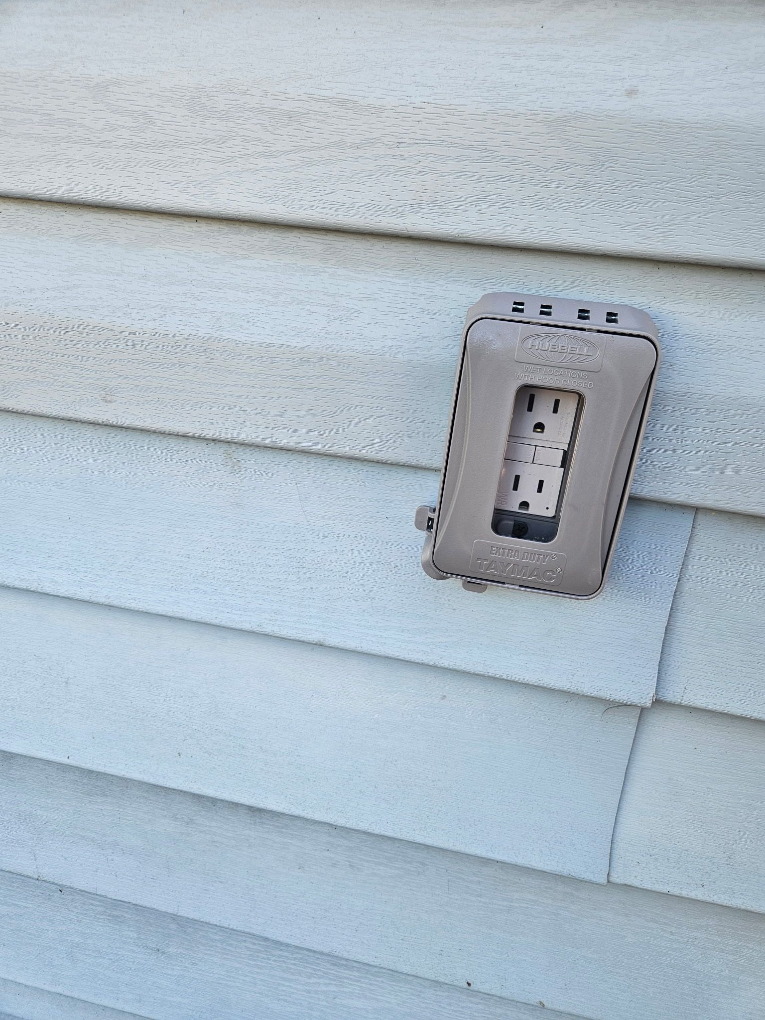Exterior GFCI outlet in a weatherproof in-use cover mounted on pale lap siding